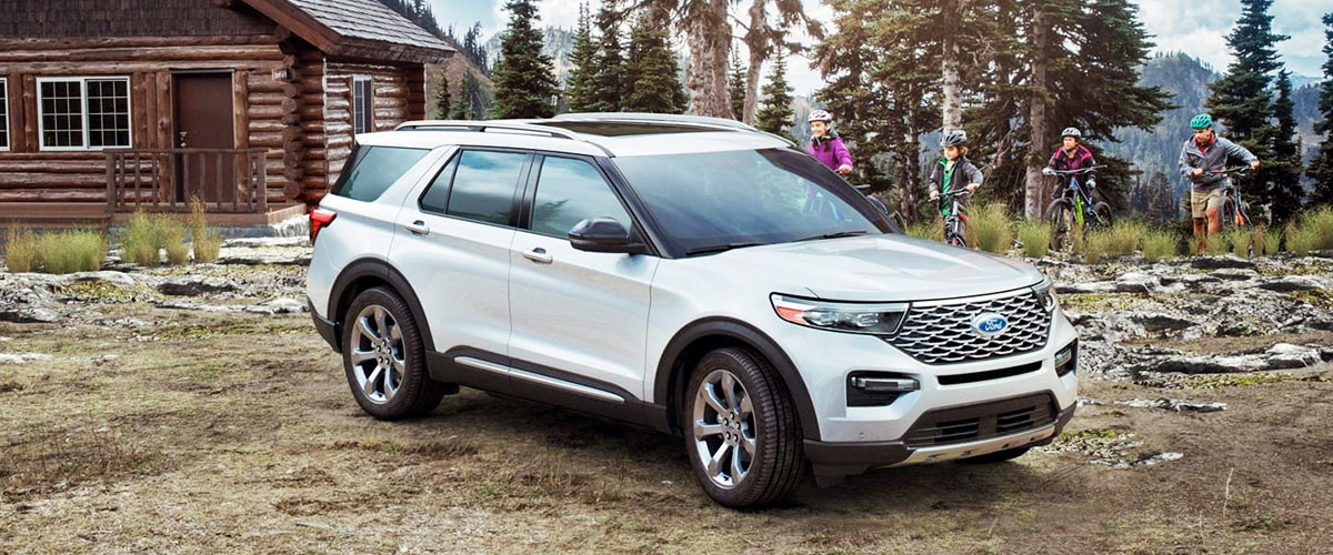 side view of a white ford explorer in front of a wood cabin sorrounded by pine trees