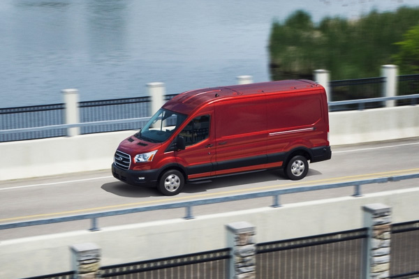 Side profile of a red 2020 Ford Transit van driving across a bridge