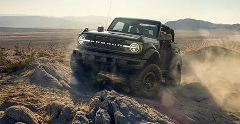 2021 Ford® Bronco two door Badlands™ in Shadow Black with available modular front bumper traveling over rugged terrain