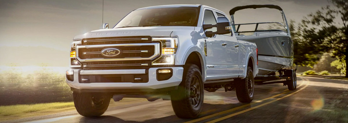 2021 Ford Super Duty in Star White towing boat on road alongside water