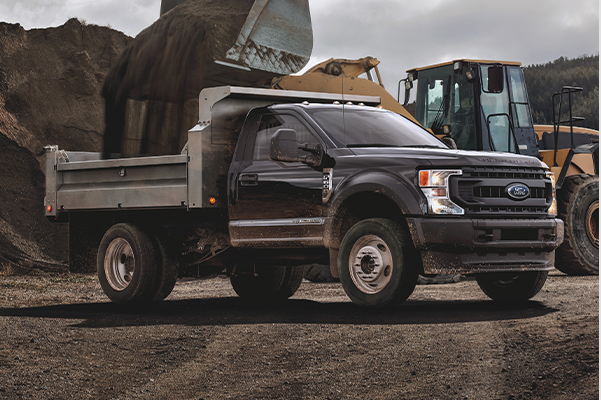 2021 Ford Super Duty® F-600 parked in a construction zone with a front loader putting dirt in the truck's bed 