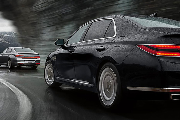 Rear shot of 2021 Genesis G90 vehicles driving through the rain on a winding road