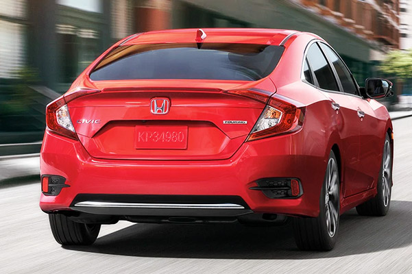 Rear view of the 2021 Civic Sport Sedan in Rallye Red driving on urban street.