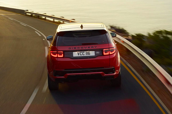 Rear view of a 2021 Land Rover Discovery Sport driving down a scenic highway