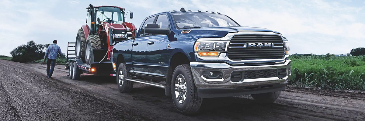 The 2021 Ram 2500 Big Horn towing a flatbed loaded with a farming tractor.