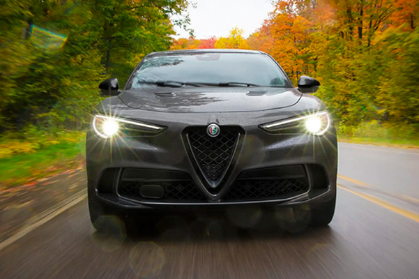 Front exterior shot of a 2022 Alfa Romeo Stelvio driving on a road in the woods.