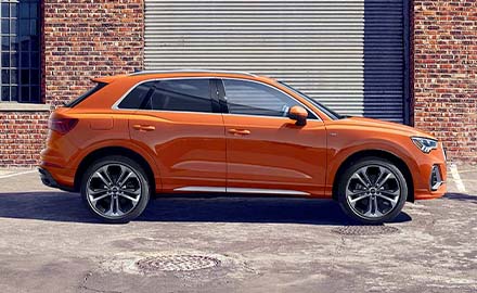 side view of the orange 2022 Audi Q3 parked in front of a building