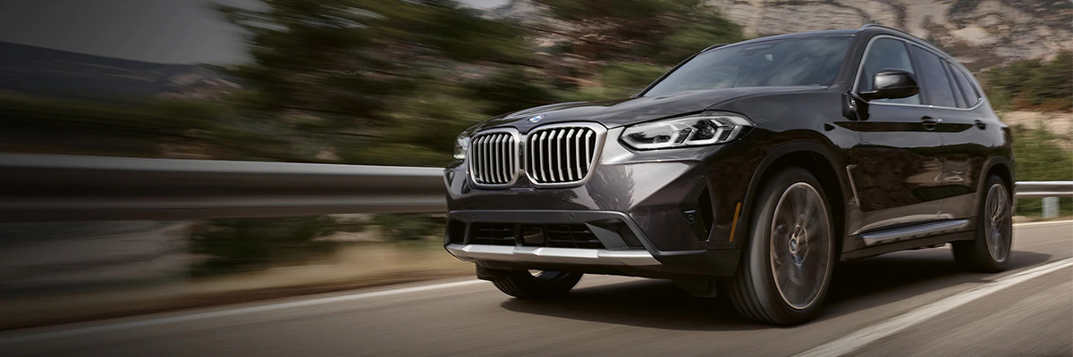 Exterior shot of a 2022 BMW X3 driving down a road during the day.
