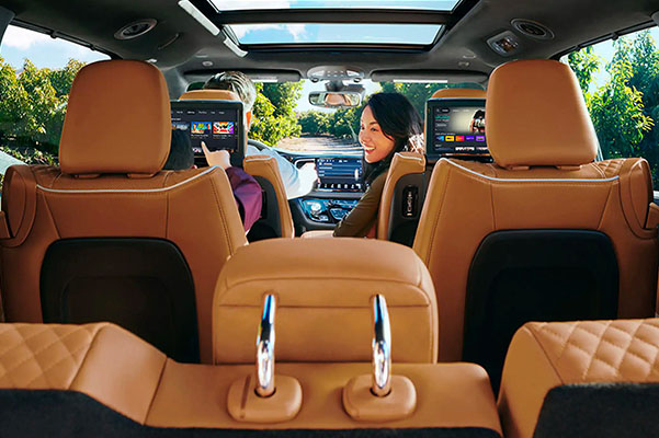 The front passenger in the 2022 Chrysler Pacifica Pacifica turning to look at a child in the second row who is browsing options on the rear seat entertainment system.
