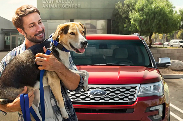 Person holding a dog standing in front of a parked Ford SUV