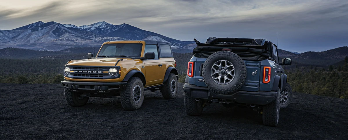 2022 Ford Broncos parked side by side on gravel overlooking mountains.