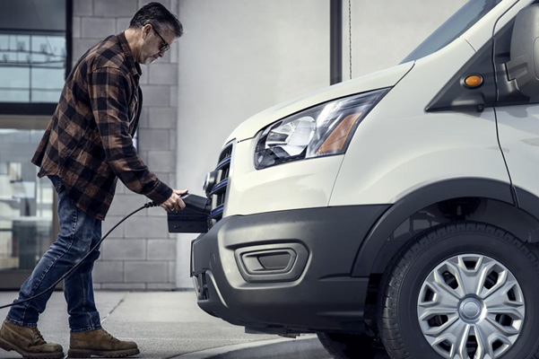 Side view of man plugging charger into the front of a parked 2022 Ford E-Transit