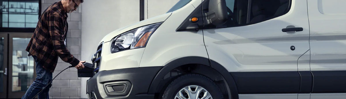 A man plugging a charger into the front of a 2022 Ford E Transit