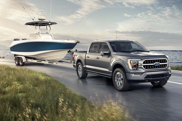 A 2021 Ford F 1 50 Platinum parked by a large body of water with a boat in tow