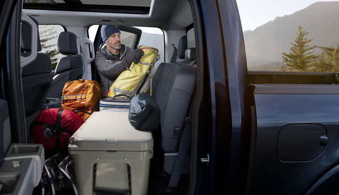 A man loading camping gear onto the rear flat load floor in a 2021 Ford F one fifty