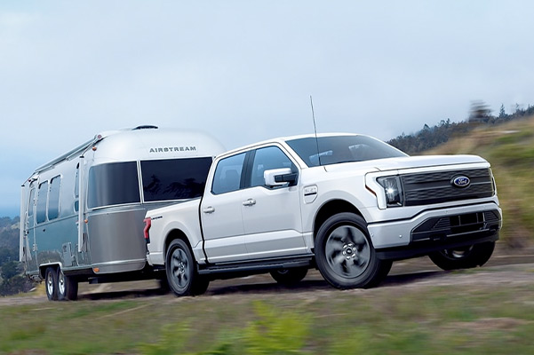 A 2022 Ford® F-150 Lightning towing a trailer near the ocean