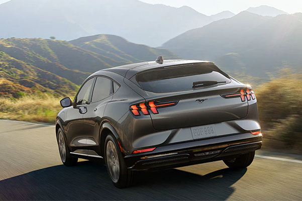 Rear view of a 2022 Ford Mustang Mach-E driving down a scenic road