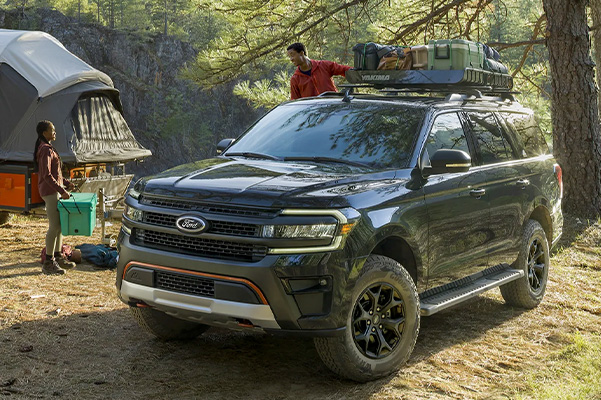 A 2022 Ford Expedition parked at a campsite with cargo on the roof racks with people nearby