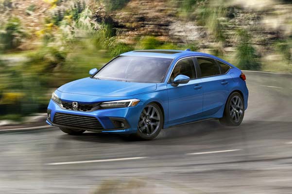 Front driver-side view of the 2022 Honda Civic Sport Touring Hatchback in Boost Blue Pearl, rounding a hairpin turn on a mountainside road.