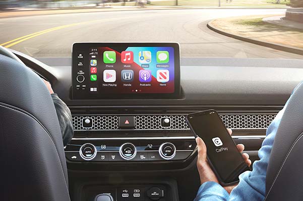 Apple CarPlay® menu on the 9-inch color touch-screen in the 2022 Honda Civic Sport Touring Hatchback with Black Leather, with front passenger holding an iPhone®.