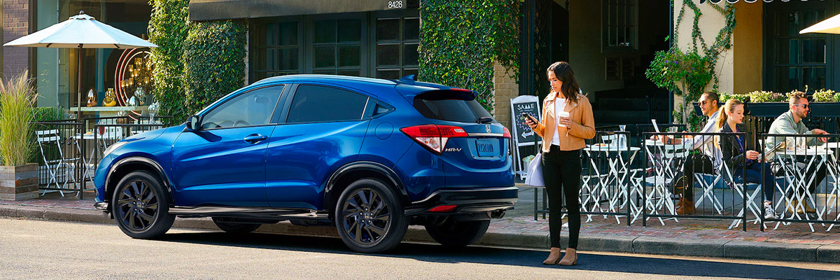 Blue 2022 Honda HR-V parked out front of a restaurant with woman answering phone with coffee in hand. 