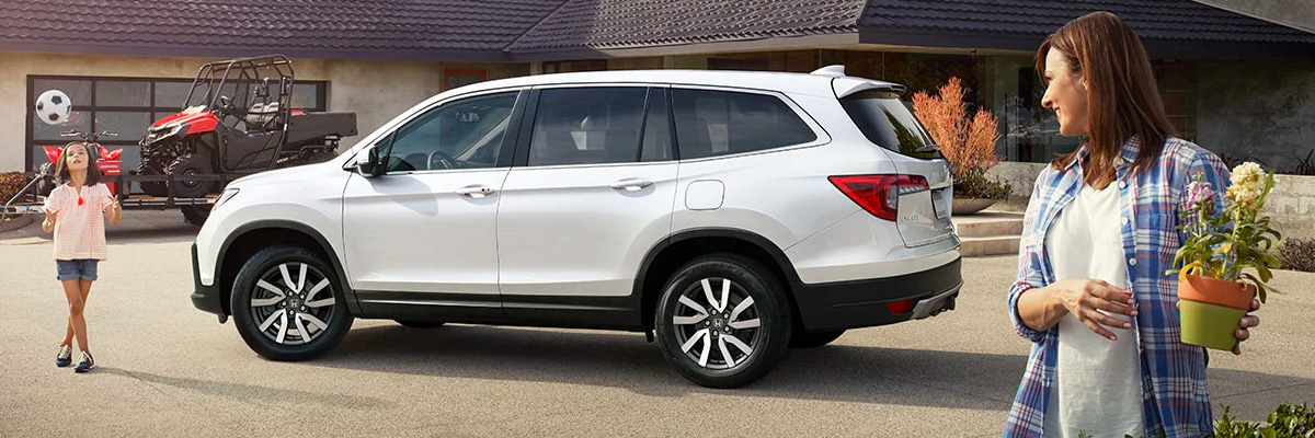 2022 Honda Pilot parked in the driveway while mom plants and daughter plays soccer