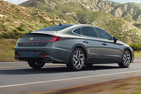 Exterior, rear shot of a 2022 Hyundai Sonata driving down a road with grassy hills in the background.