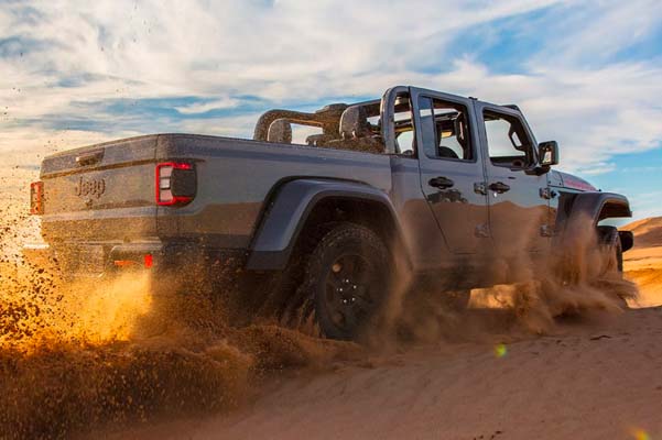 The 2022 Jeep Gladiator Mojave being driven in deep sand, a cloud of dust in its wake.