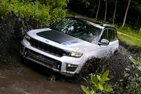 The 2022 Jeep Grand Cherokee 4xe Trailhawk splashes up mud as it’s driven through a stream.