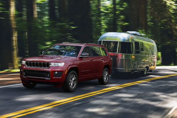 The 2022 Jeep Grand Cherokee Overland towing a streamlined camper as it’s driven through the woods.