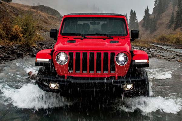 The 2022 Jeep Wrangler driving straight ahead through shallow water in the rain