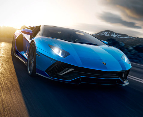 Exterior shot of the front of a Lamborghini Aventador LP 780-4 Ultimae Roadster driving on a road with mountains in the background.
