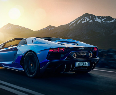 Rear, exterior shot of a Lamborghini Aventador LP 780-4 Ultimae Roadster driving down a road with mountains in the background.