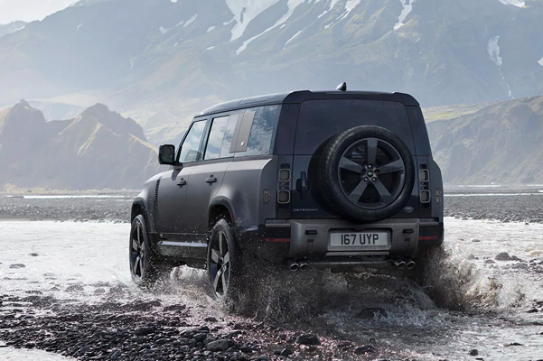 2022 Land Rover Defender driving through a puddle with mountains in the background