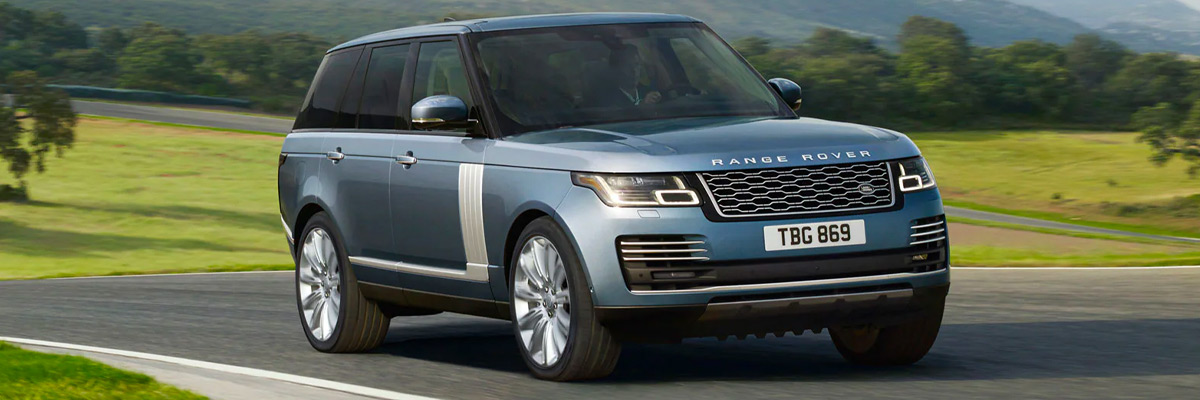 Exterior shot of a 2022 Range Rover driving on a road with a grassy field and trees in the background.