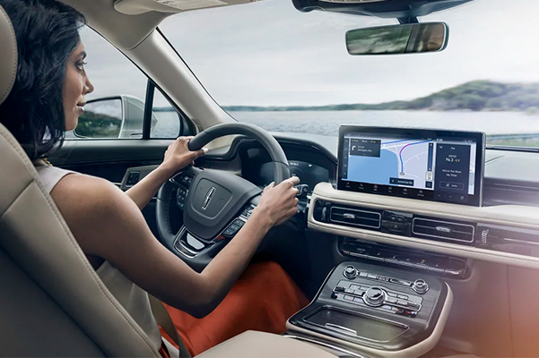 A woman is driving a 2022 Lincoln Nautilus as the navigation application on the center touchscreen guides her course