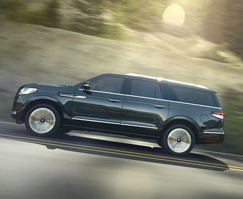 A 2022 Lincoln Navigator in Flight Blue is being driven along a road as shadows emphasize the curvature and sculpted profile