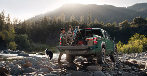 The 2022 Nissan Frontier parked on rocks with the truck bed opened holding a bike and stoarge containers