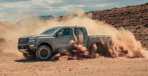 The 2022 Nissan Frontier driving on a dirt path, with dirt being kicked up around the vehicle