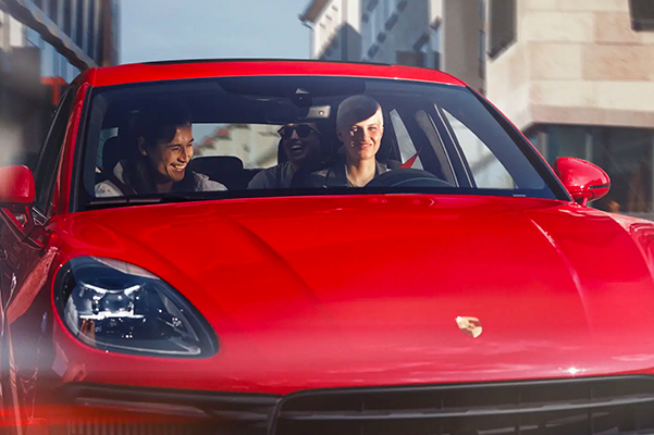 Front shot of a red 2022 Porsche Macan with a driver and passengers in the vehicle.