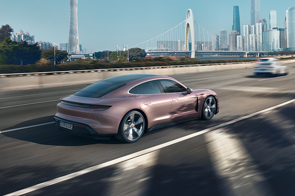 Exterior shot of a 2022 Porsche Taycan driving on the highway towards a city.