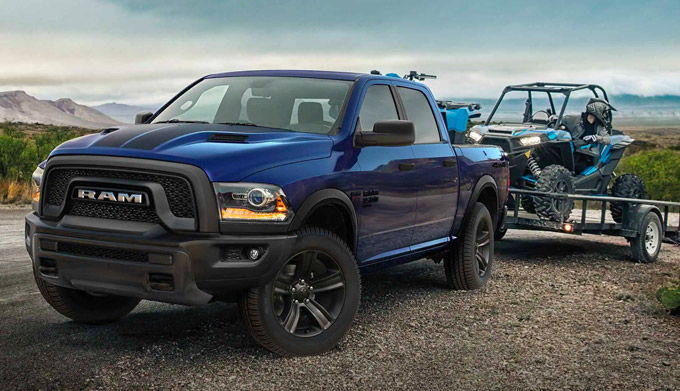 Display A 2022 Ram 1500 Classic hitched to a flatbed trailer with an ATV on it.