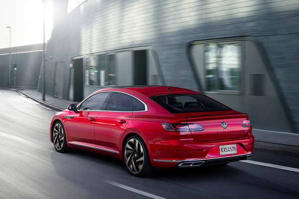 Arteon shown in Kings Red Metallic from rear driving on a modern city street