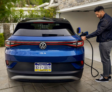 A man plugs an ID.4 (shown in Dusk Blue Metallic) into an at-home charging station.