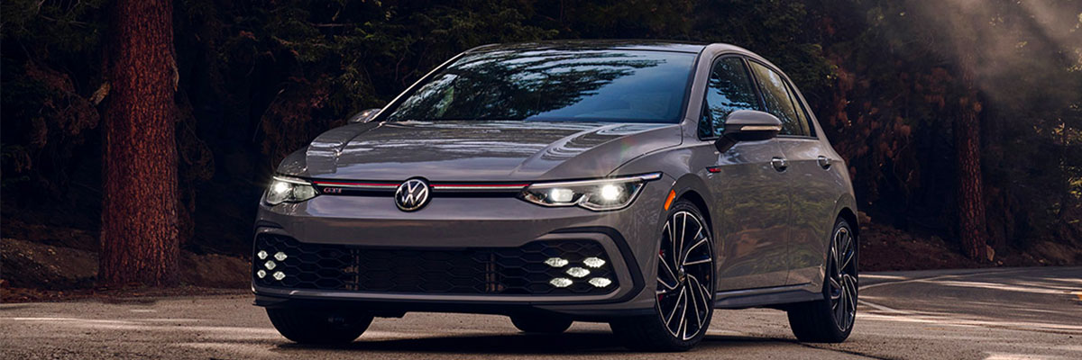 Golf GTI shown in Moonstone Gray from the front, pulling off a tree-lined road at dawn