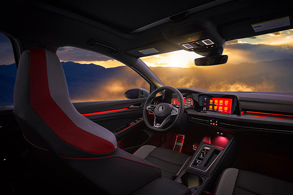 Red ambient lighting glows along the door, dash, center console, and footwells of driver’s side cockpit