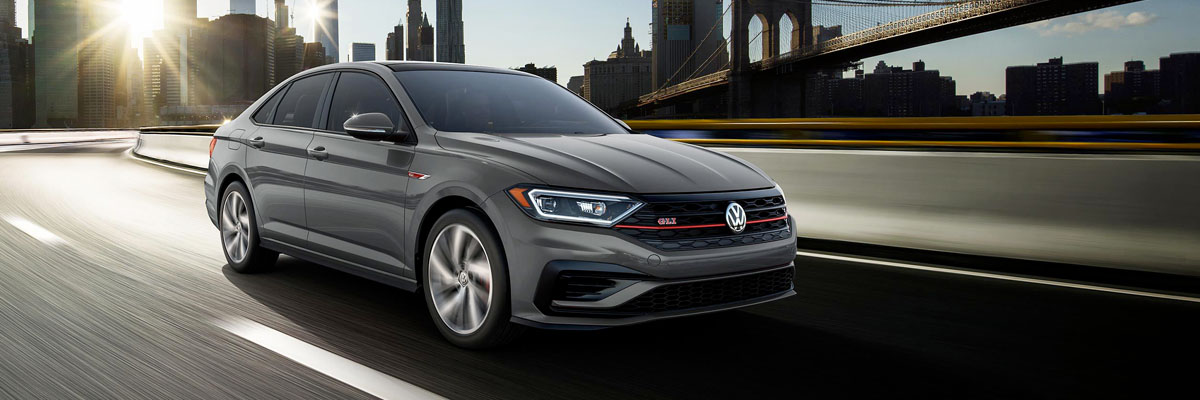 Jetta GLI in Pure Gray driving away from the city. Color adds an additional $295 to price of car.