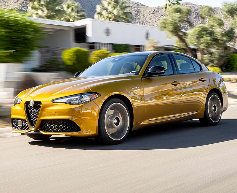 A gold 2023 Alfa Romeo Giulia Veloce being driven on a street with mountains in the distance, the background is blurred to indicate the speed of the vehicle.