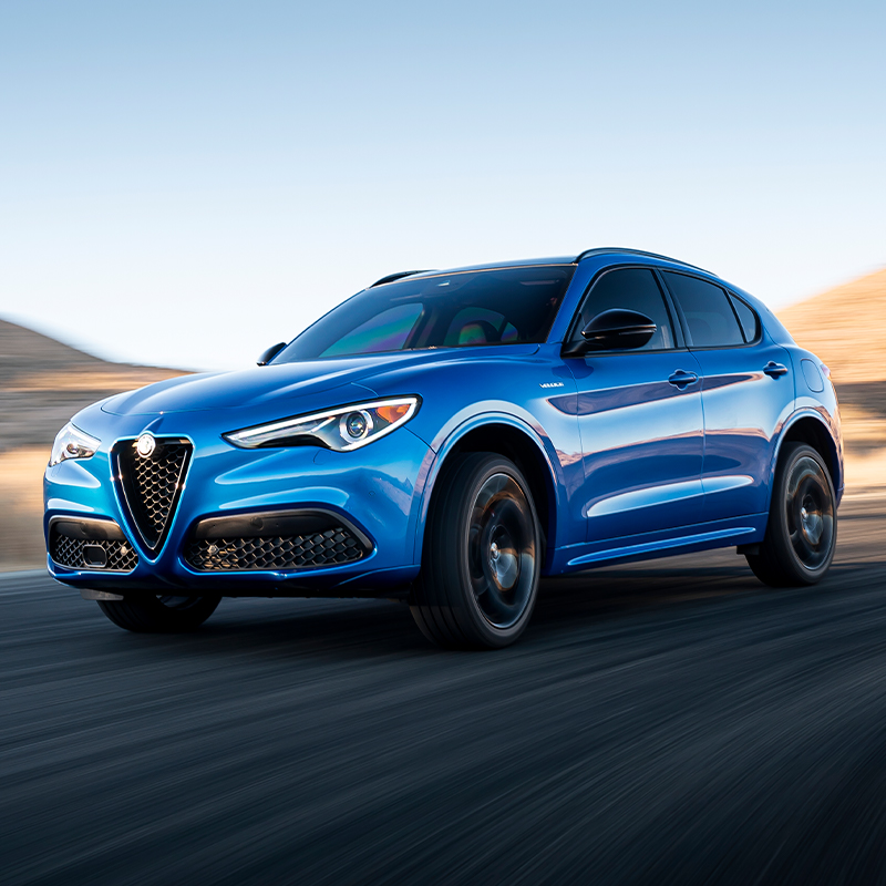 2023 Stelvio Veloce in Misano Blue Metallic driving around curved desert road with hills and clear skies in the distance.