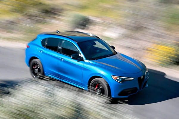 The 2023 Alfa Romeo Stelvio driving through a street surrounded by blurred bushes and trees